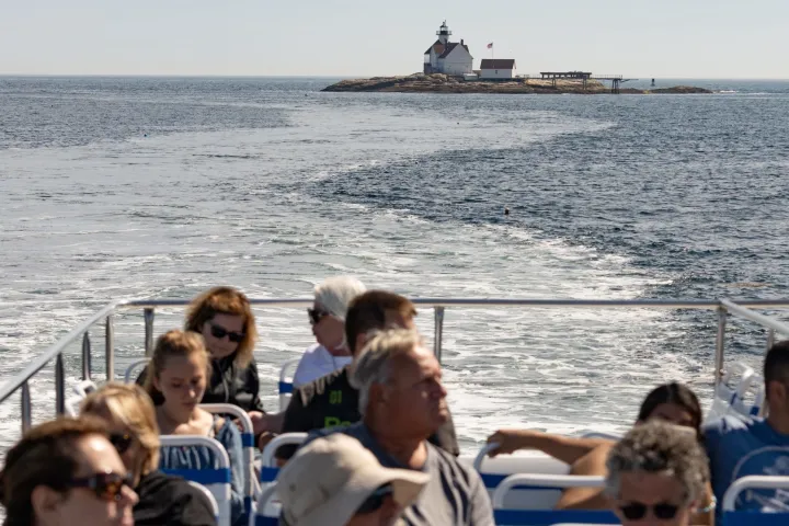 group of people on a boat looking at a Maine island and lighthouse