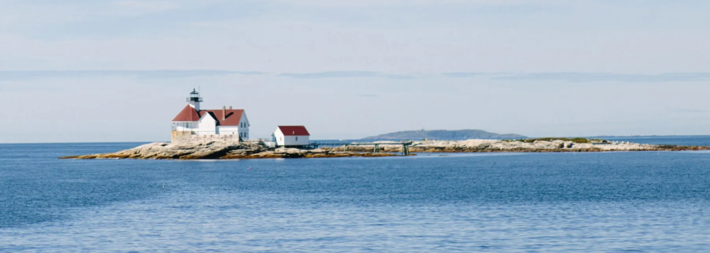 Lighthouse on a small rocky island surrounded by calm blue sea.